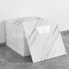 A stack of rectangular faux marble 3D self-adhesive wall tiles with white veining displayed on a gray floor.
