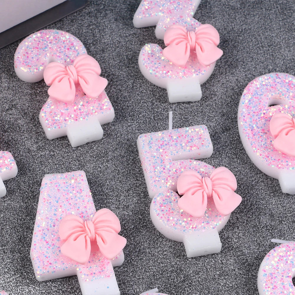 Pink glitter number cake candles shaped like a number with a bow on a gray background