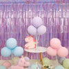 A backdrop featuring purple metallic foil tinsel fringe, pink and blue balloons, and a pink unicorn plush toy.