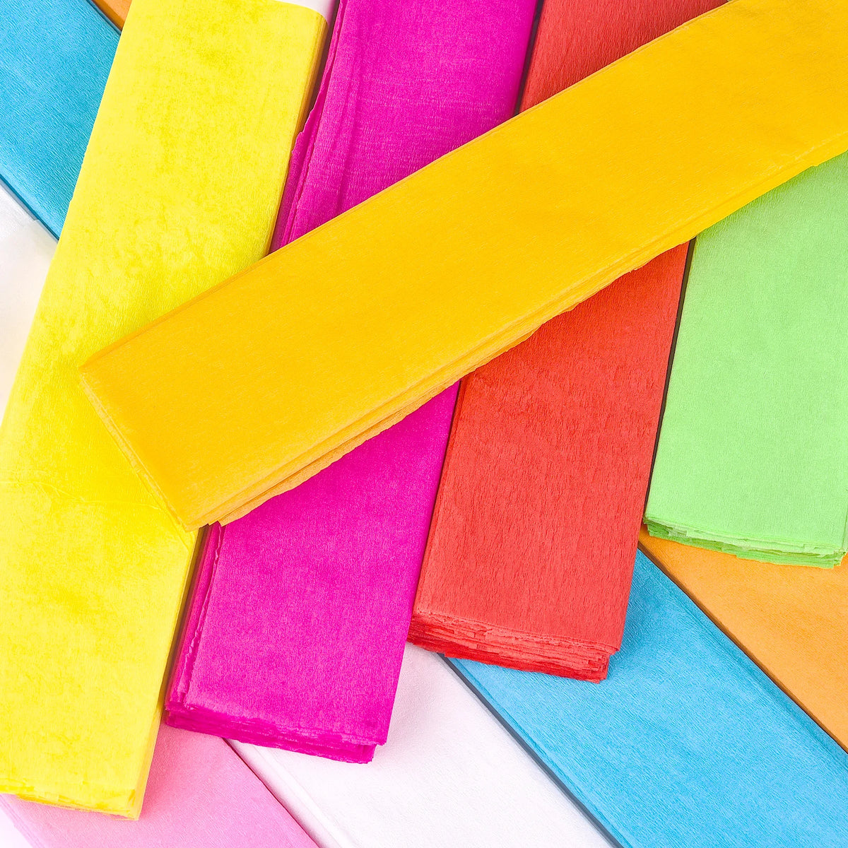 A vibrant assortment of ten colored crepe papers in various shades including yellow, pink, orange, green, and blue.