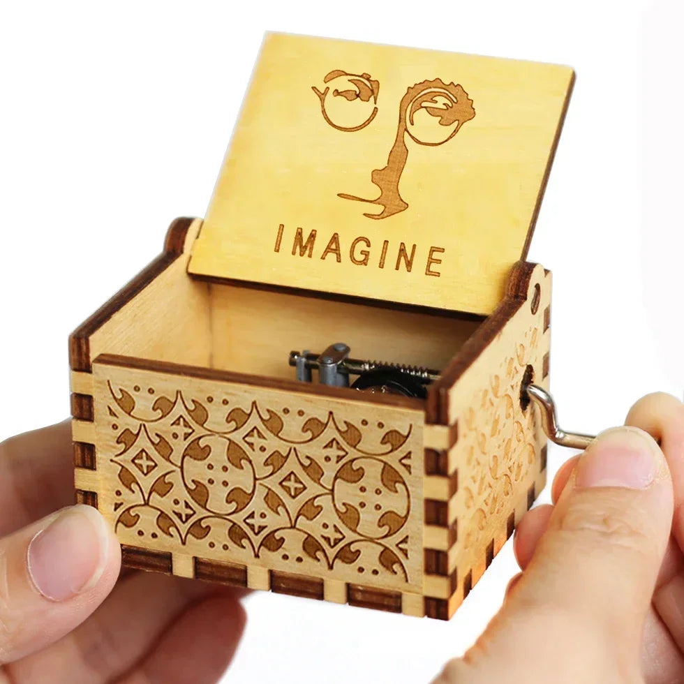 An antique engraved wooden music box with a lid featuring the word IMAGINE is held in a hand.