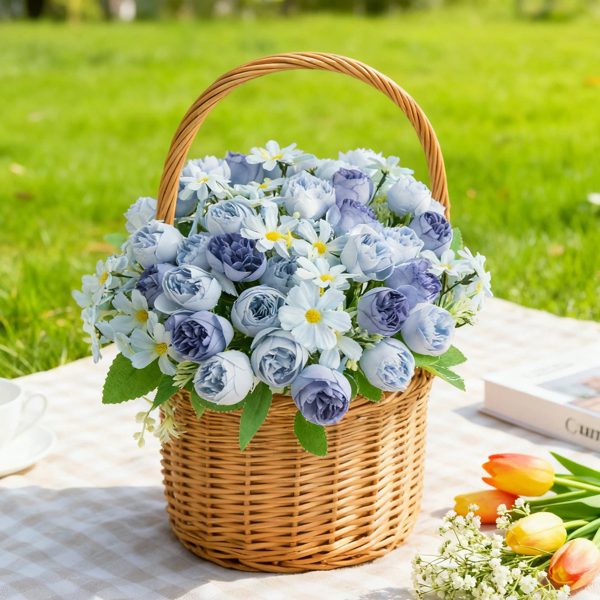 Cesta tejida llena de un ramo de flores artificiales de seda azules y moradas sobre un paño blanco.