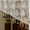 A sheer white lace valance curtain with beaded fringe hanging in a window.