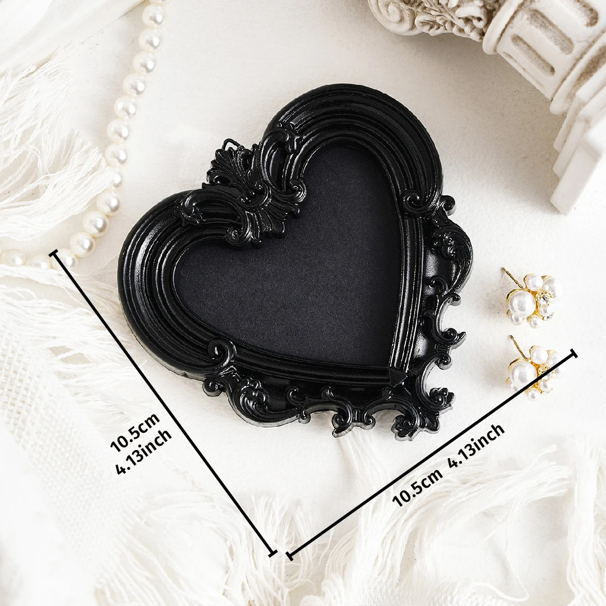 Black heart-shaped resin wall decor pendant with ornate edges shown on a white fabric background.