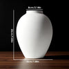 A white ceramic vase with a smooth, rounded shape is shown on a wooden surface.
