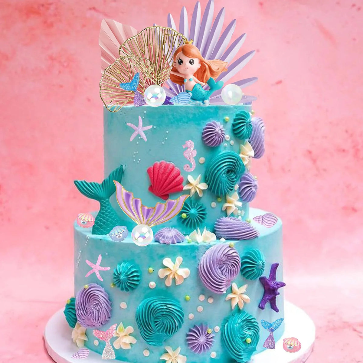 A tiered mermaid cake decorated with teal frosting, featuring sea creatures like fish tails, shells, and purple accents.