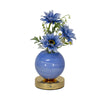 A vase filled with blue delphinium flowers sits on a gold base.