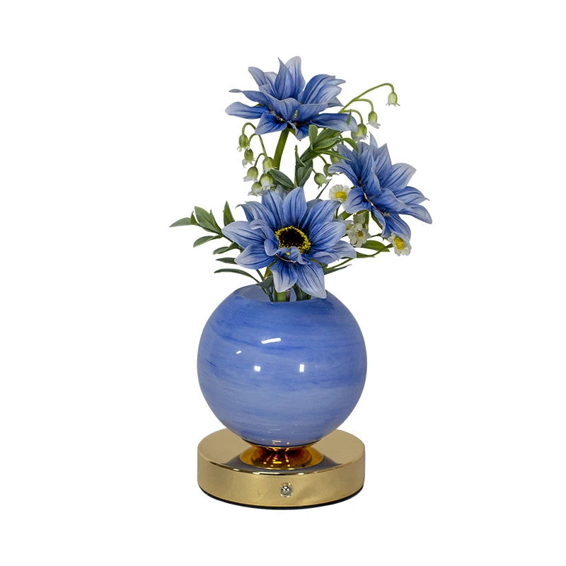 A vase filled with blue delphinium flowers sits on a gold base.