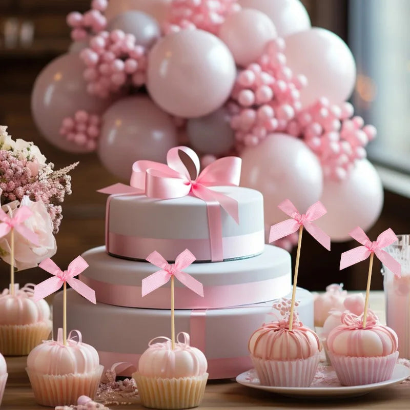 A tiered pink cake display featuring pink bow cupcake toppers and pink balloons for a celebration.