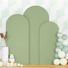A set of three sage green spandex wedding arch covers displayed on a wooden surface.