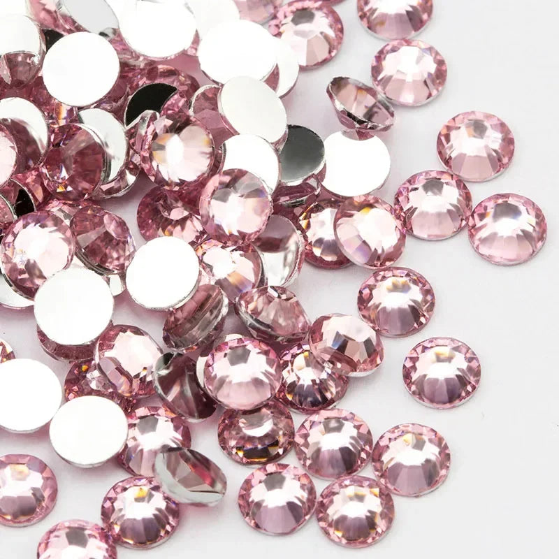 A close-up view of pink and clear round flatback resin rhinestones scattered on a white background.