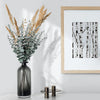 Dried beige floral arrangement in a dark vase next to a framed black and white birch tree print