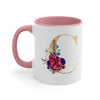 A pink ceramic coffee mug featuring a large gold letter C decorated with colorful floral accents.