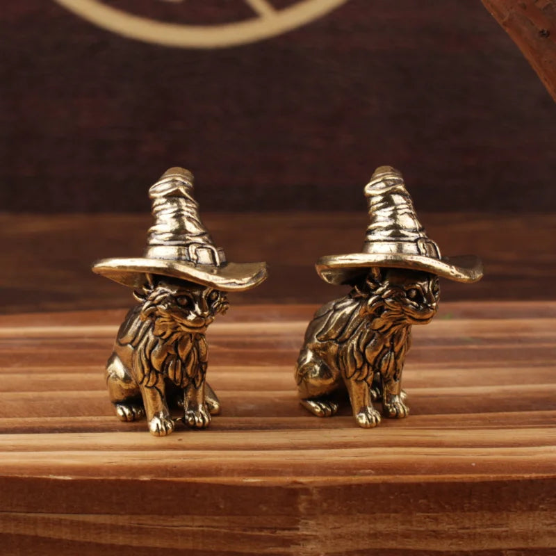 Une paire de statuettes de chats en laiton vintage portant des chapeaux à larges bords, posées sur une surface en bois.