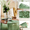 Sage green gauze table runner draped over a wooden table with a floral arrangement in a glass vase.