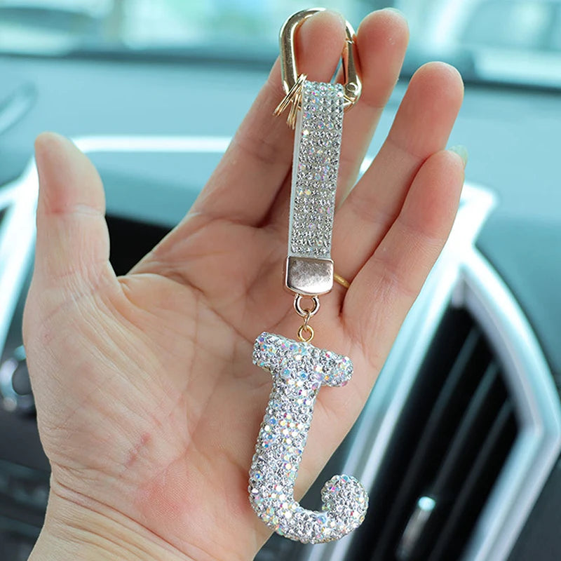 A hand holds a crystal letter keychain charm shaped like the letter J.