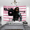 A pink American flag tapestry wall hanging displayed above a bed with a person in a leather jacket.