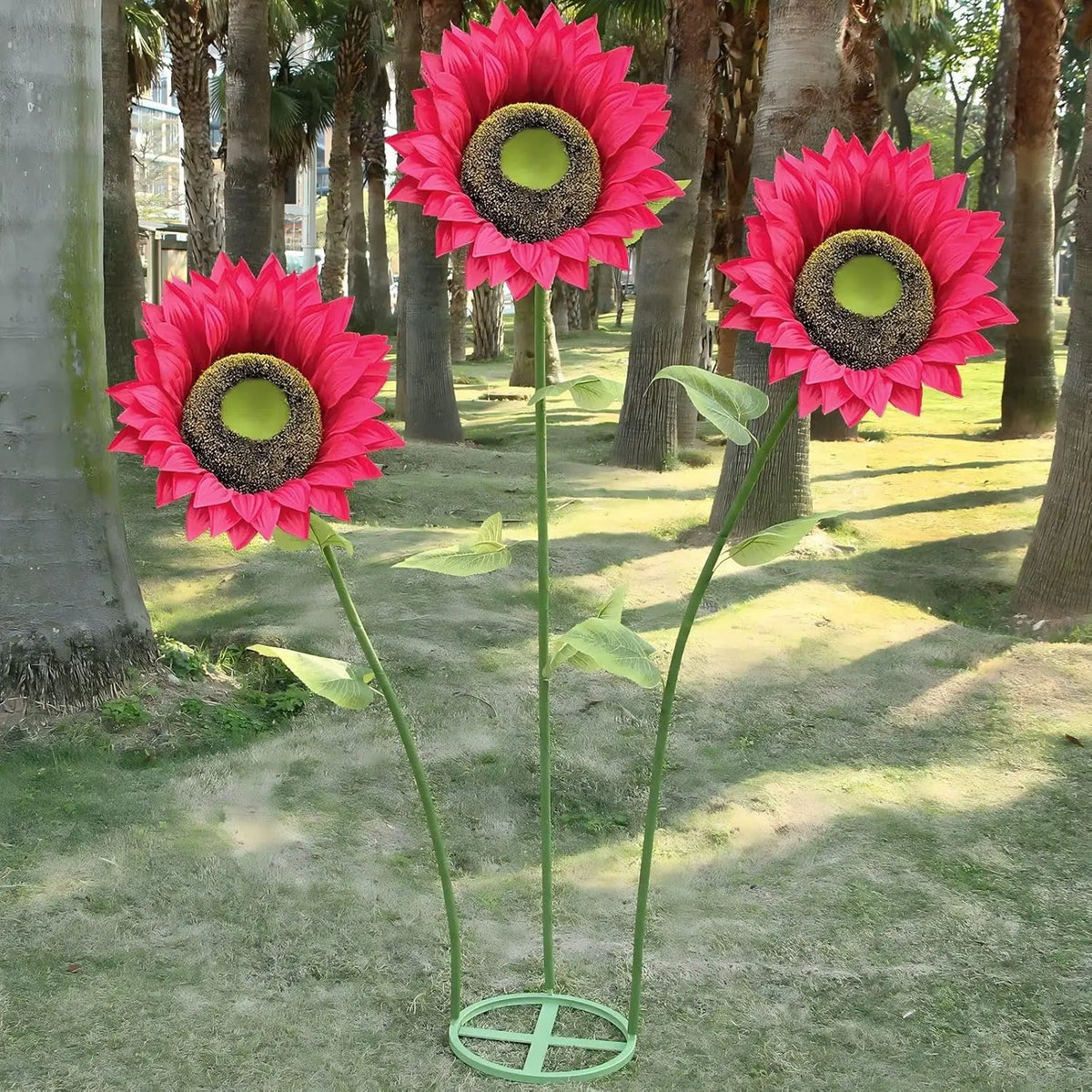A vibrant pink and red giant silk sunflower with a dark center is displayed in an outdoor setting.