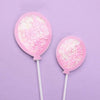 A pink cake topper set featuring two pink lollipop-like items on white sticks against a light purple background.