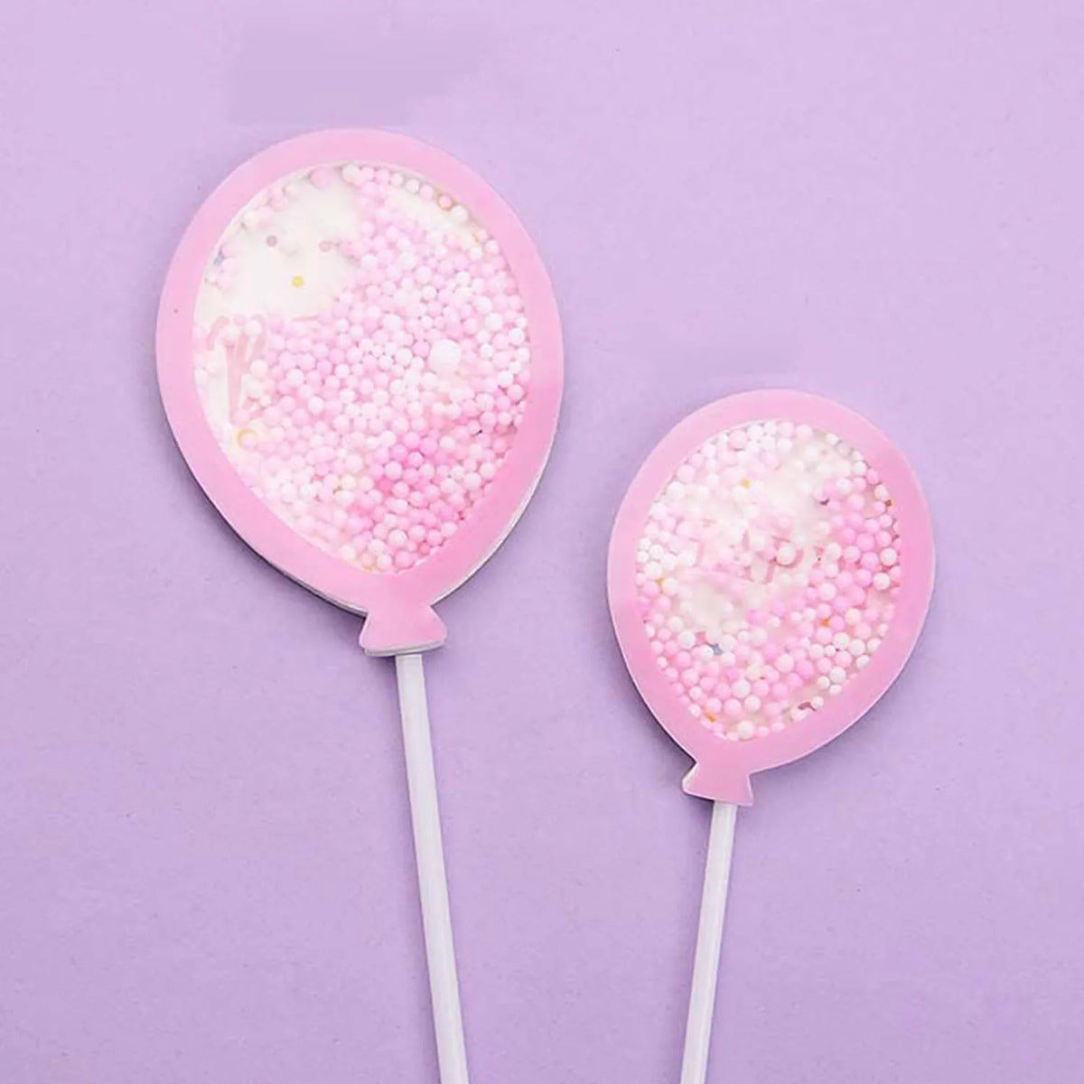 A pink cake topper set featuring two pink lollipop-like items on white sticks against a light purple background.