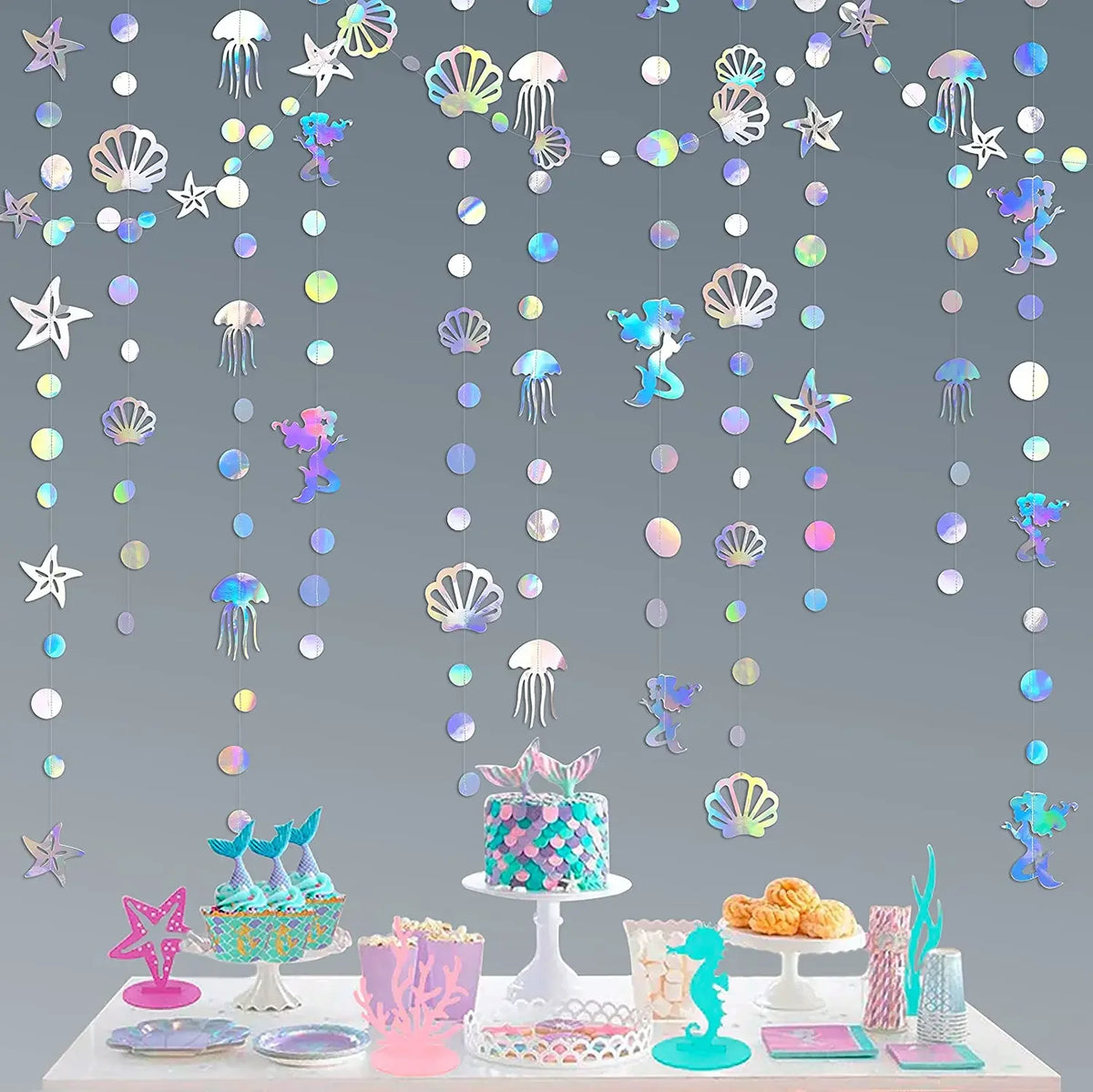 Iridescent mermaid and jellyfish party streamers hanging against a gray background with treats.