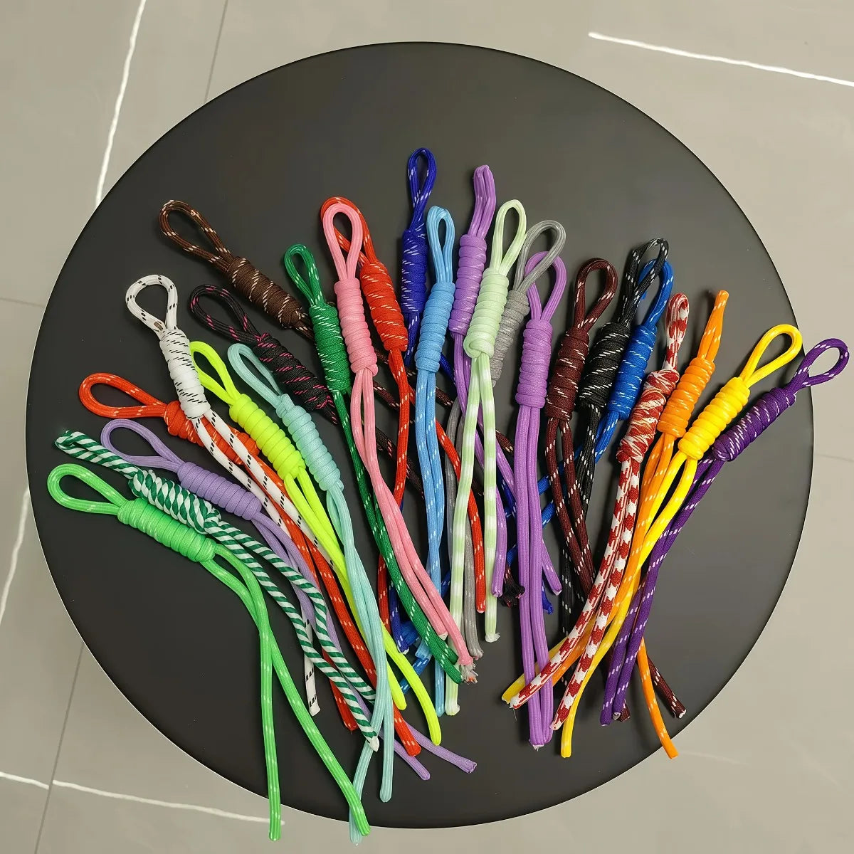 A collection of colorful nylon ropes in various shades and textures laid out on a dark circular surface.