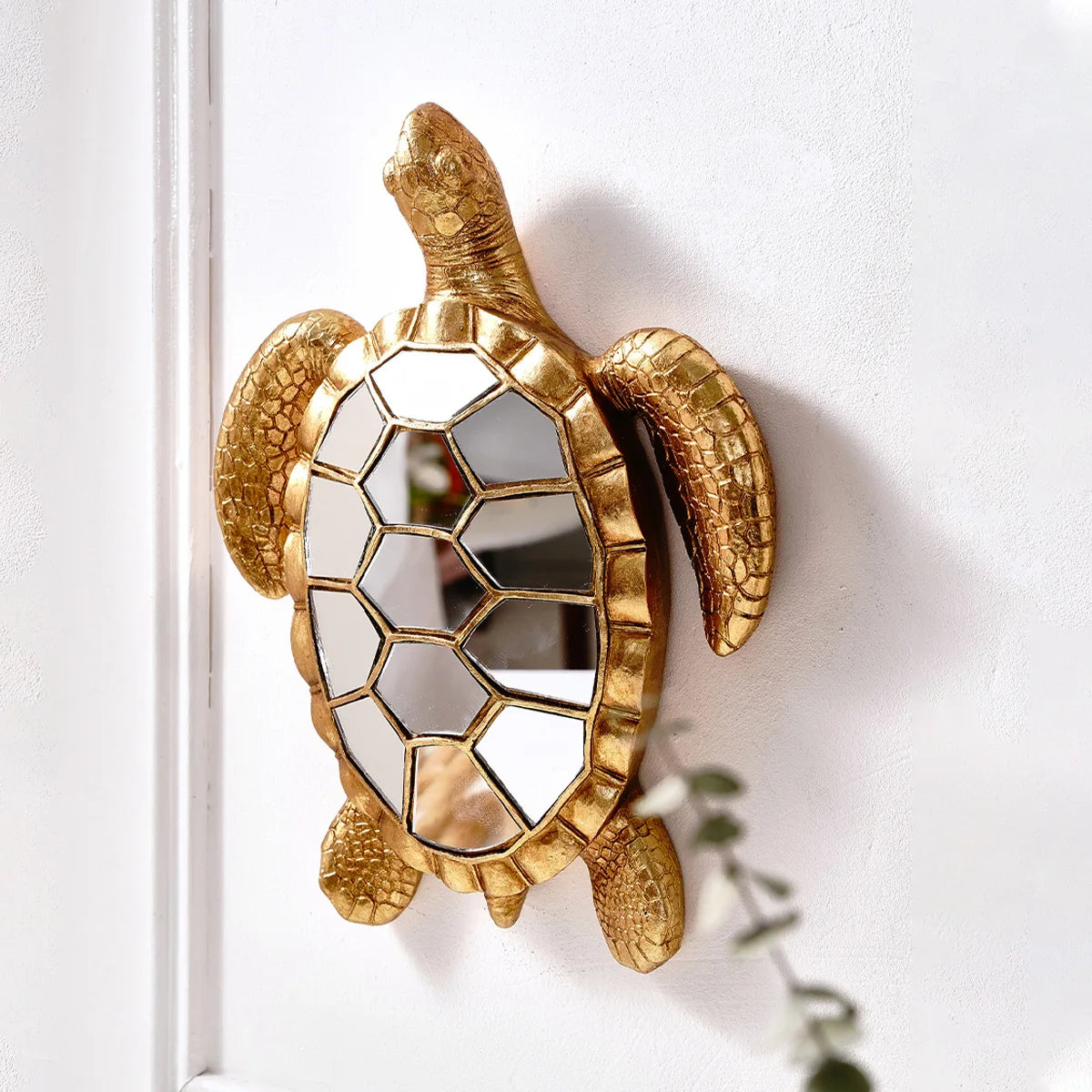 A golden sea turtle resin wall decor mirror mounted on a white wall.