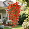 A vibrant cascade of red artificial morning glory vine hanging outdoors near a house.