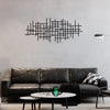 A dark leather sofa sits in front of a gray wall featuring a black geometric metal wall art sculpture.