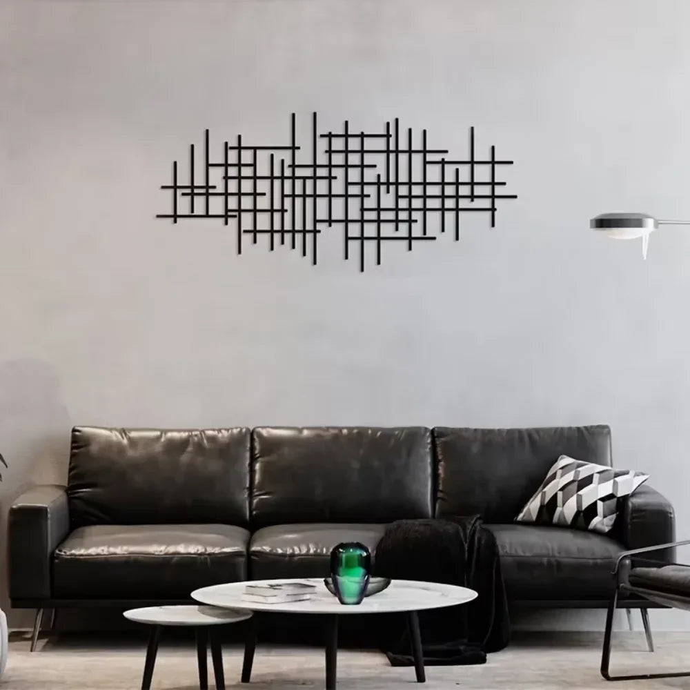 A dark leather sofa sits in front of a gray wall featuring a black geometric metal wall art sculpture.