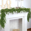 Green Norfolk pine Christmas garland draped across a white fireplace mantel