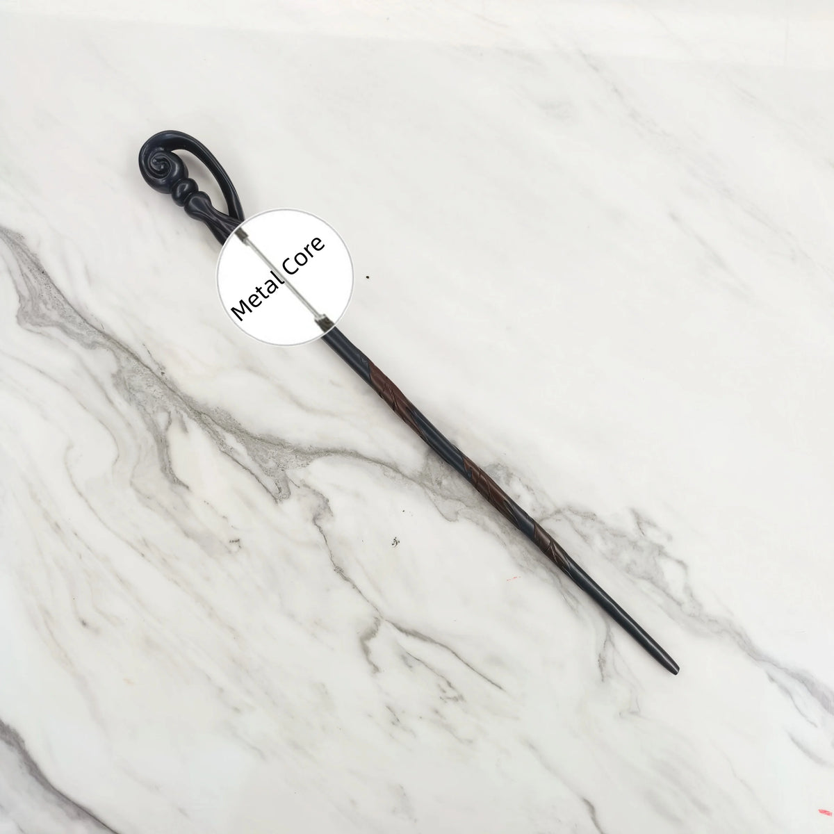 A dark metal magic wand replica with an ornate handle and a pointed tip resting on a white marble surface.