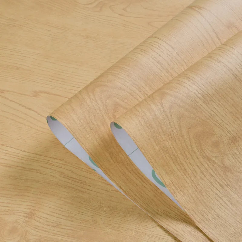 Roll of self-adhesive PVC wallpaper film with a wood grain texture shown on a wooden surface.