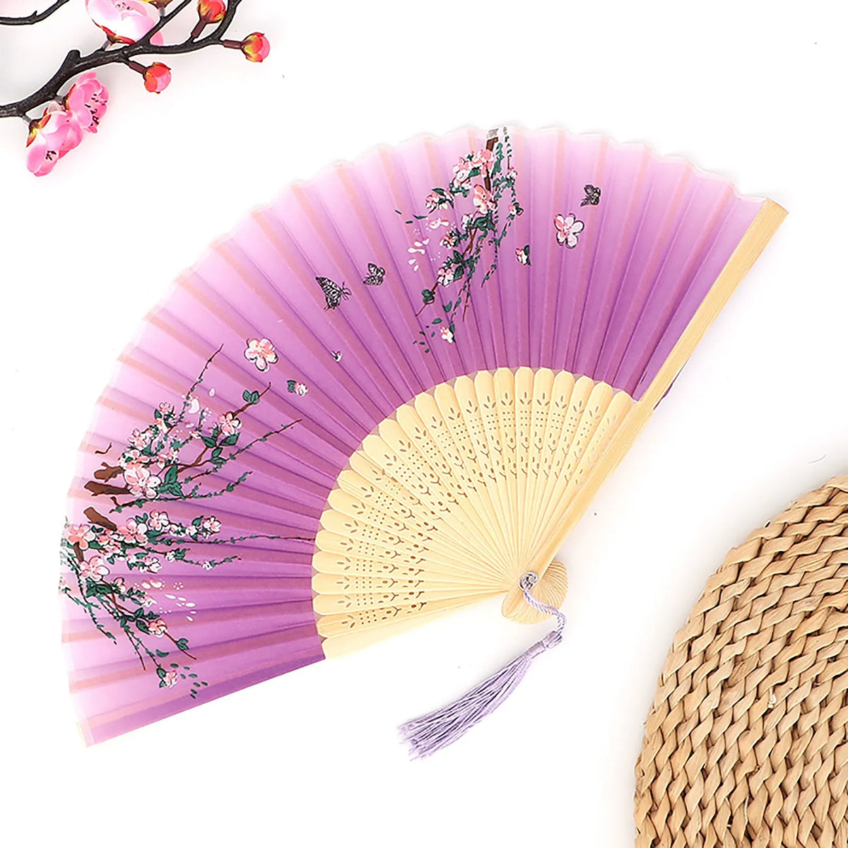 A vintage bamboo folding fan with purple fabric and pink floral accents, shown partially open.