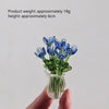 A hand holds a small bouquet of blue glass flowers in a clear glass vase.