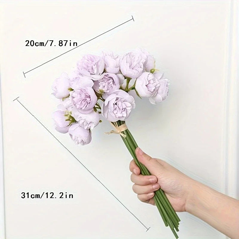 A hand holds a bouquet of light purple silk peonies against a white background.
