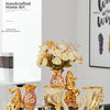A pair of gold-plated ceramic swan vases displayed on a white surface with floral arrangements.