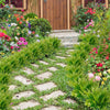 A garden path lined with bright green artificial Boston ferns and colorful flowering plants leading to a wooden door.