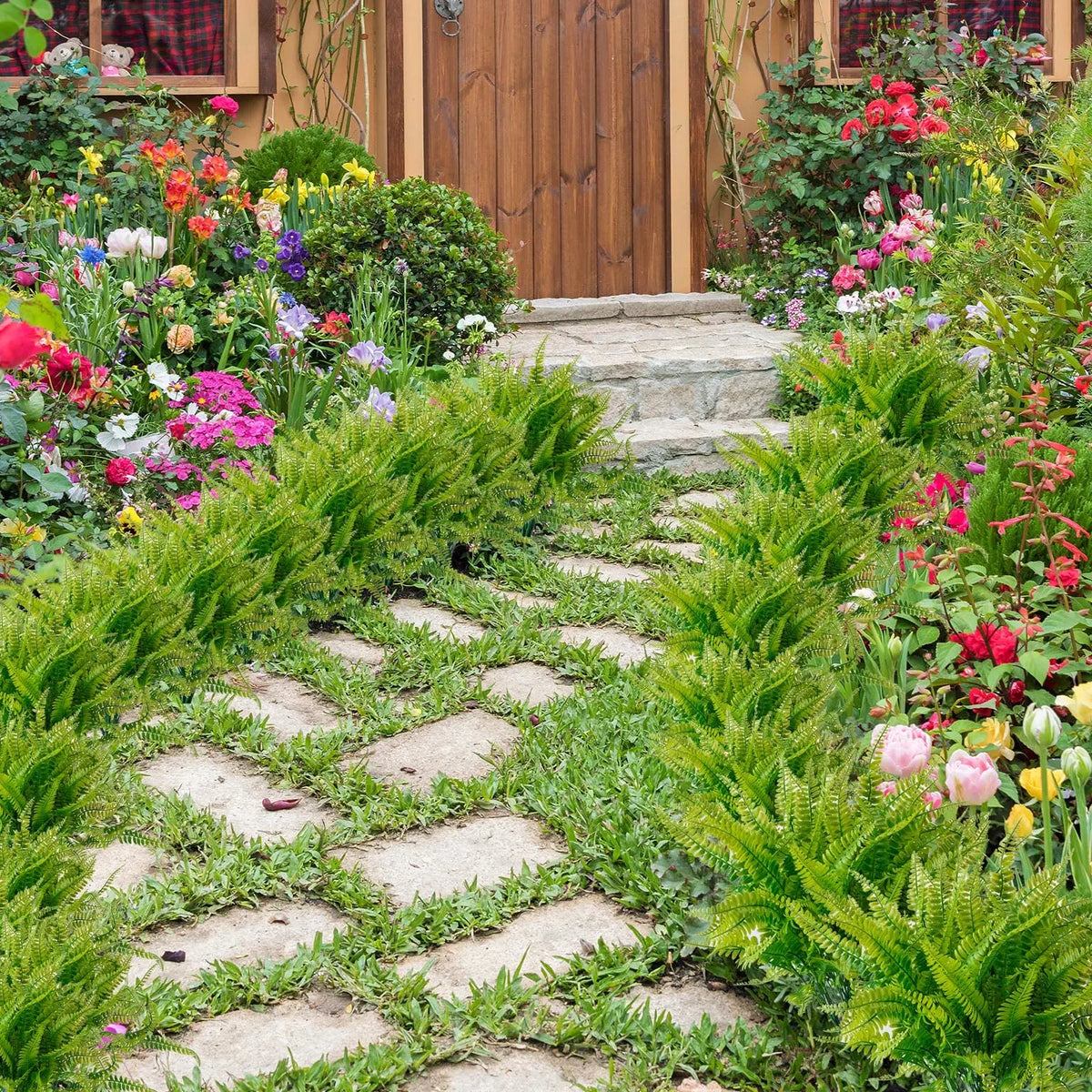 A garden path lined with bright green artificial Boston ferns and colorful flowering plants leading to a wooden door.