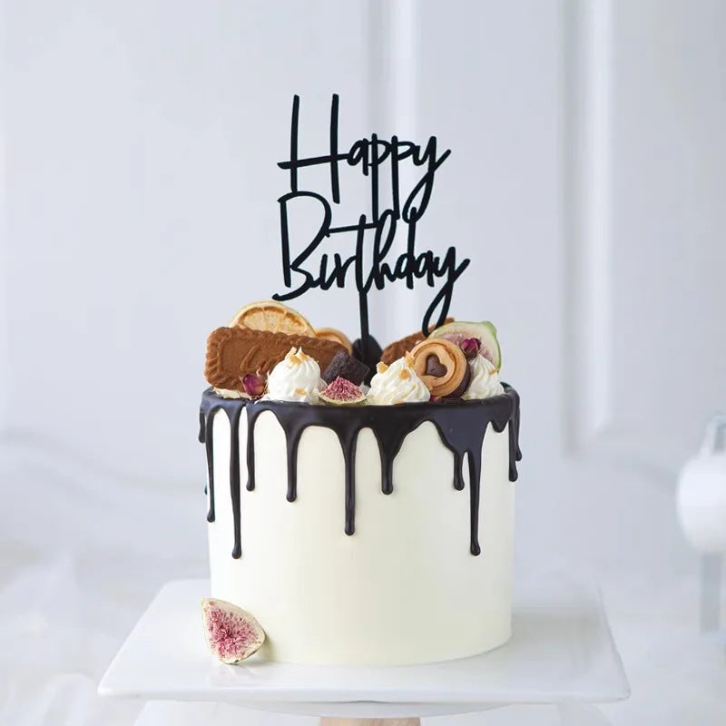 A white birthday cake with chocolate drip and black lettering on top, decorated with various cookies.