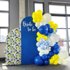 A vertical display of round latex balloons in yellow, white, and blue, with a blue backdrop and a patterned panel.