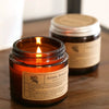A hand-poured soy aromatherapy candle in a glass jar with a lit wick, set against a wooden surface.
