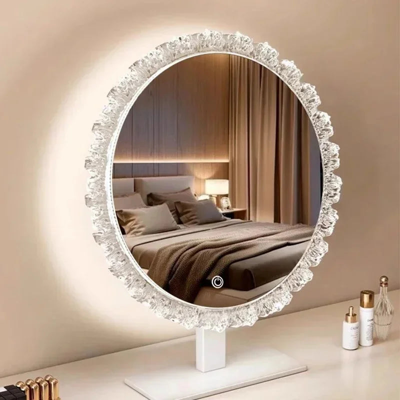 Round, ornate LED vanity mirror with illuminated glass framed in white lace, resting on a white stand.