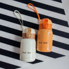 An orange vacuum insulated coffee mug with a beige lid and orange cord rests on a black and white striped surface.