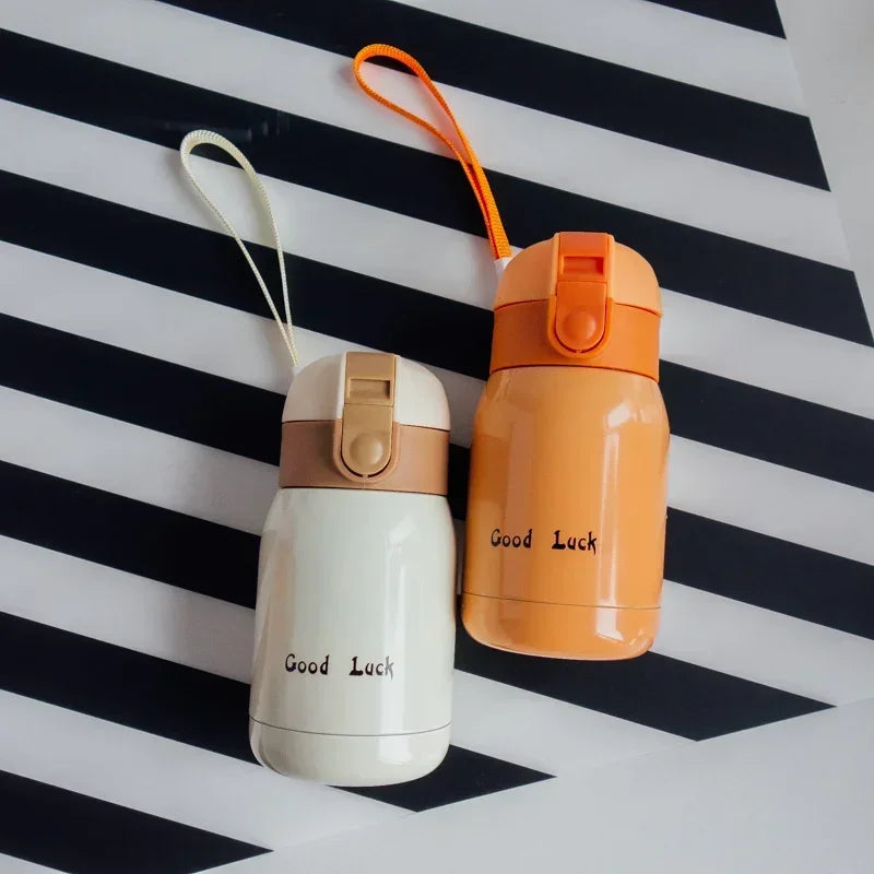 An orange vacuum insulated coffee mug with a beige lid and orange cord rests on a black and white striped surface.