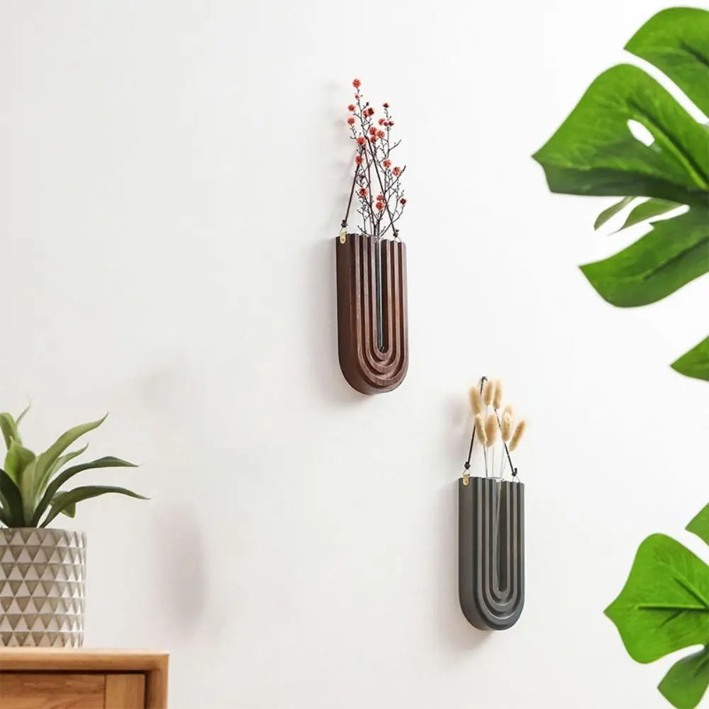 A dark brown wall-mounted vase holding delicate red branches, displayed on a white wall.