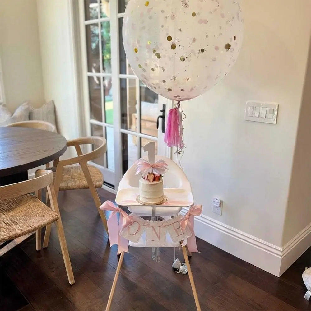 A pink and gold decorative birthday garland featuring a cake on a stand for a first birthday celebration.