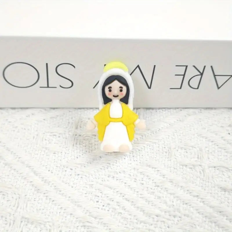 A small resin statue of the Virgin Mary with a yellow halo and robe, displayed on a white textured surface.