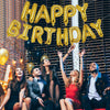 A group of five people celebrating with a large golden foil balloon banner in front of a wire mesh background.