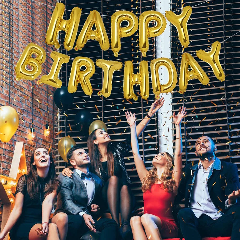 A group of five people celebrating with a large golden foil balloon banner in front of a wire mesh background.